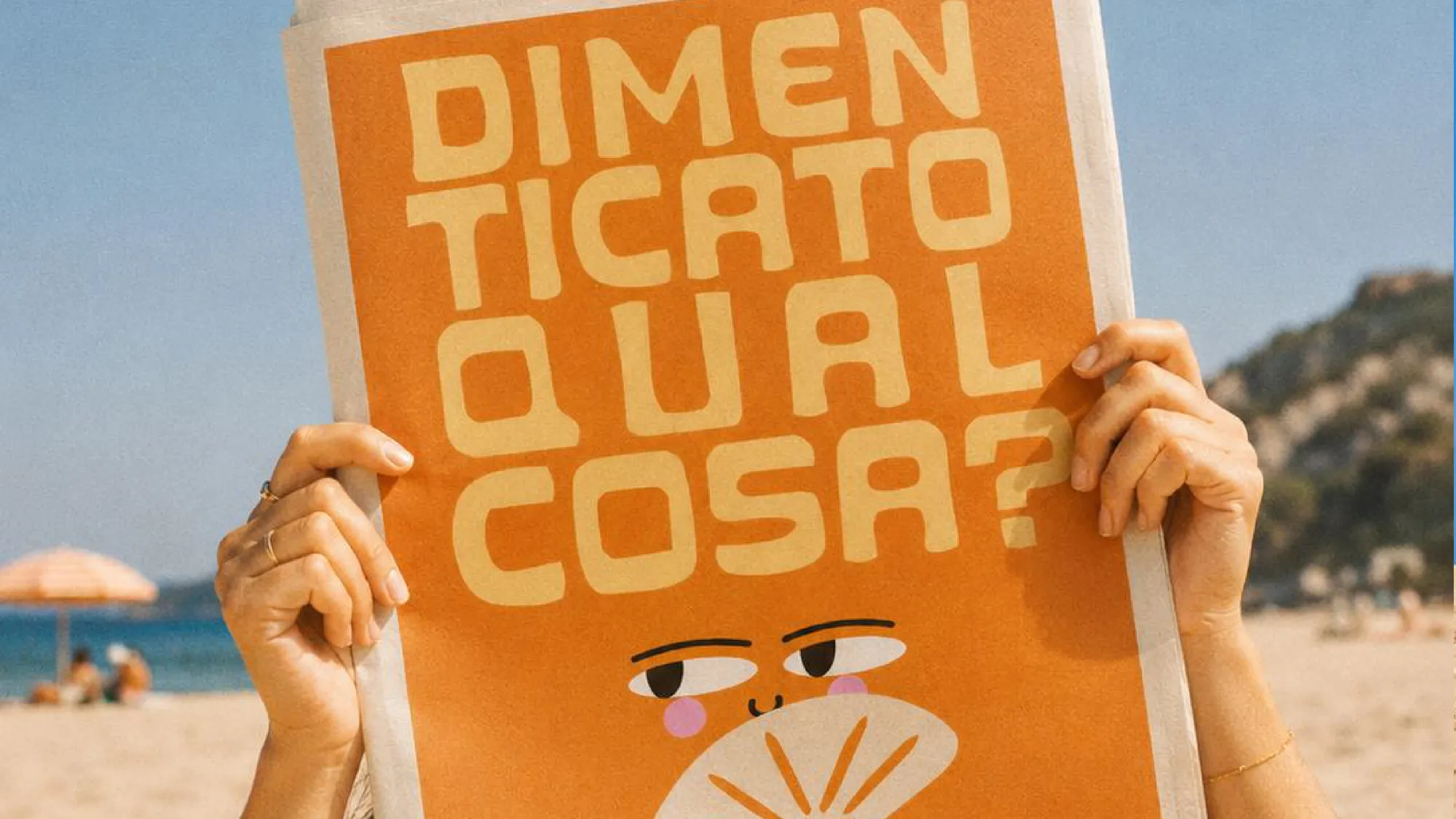 Due mani tengono un poster arancione con la scritta Dimenticato qualcosa? in spiaggia